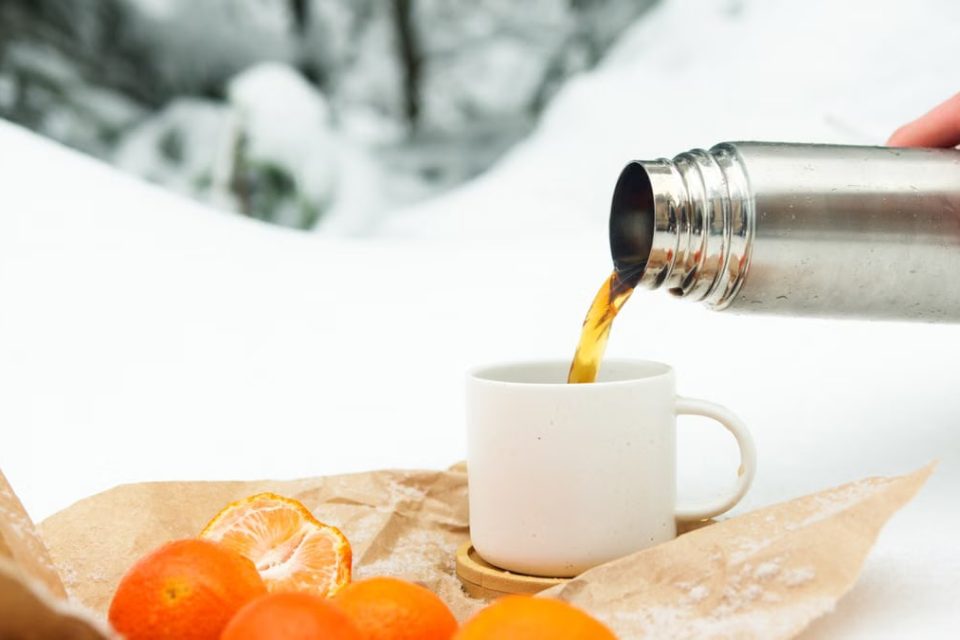 Pouring hot drink from thermos during a snowy winter picnic with oranges.