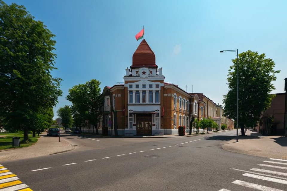 An empty street featuring a historic building with a red flag under a clear sky.